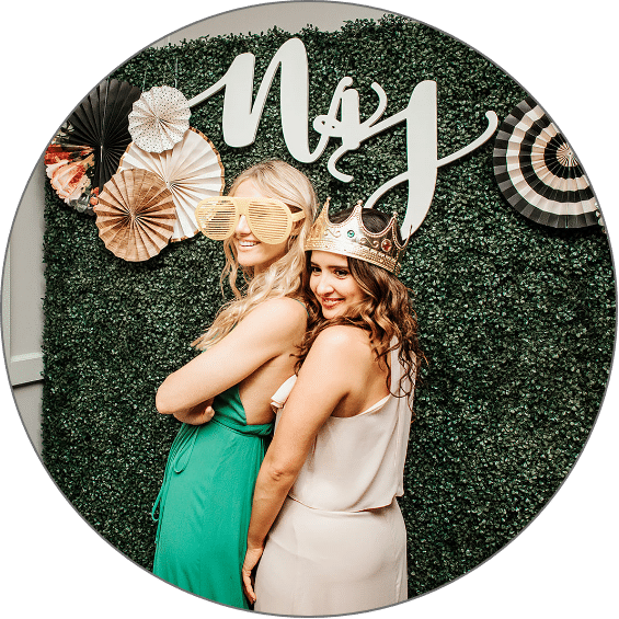 Women pose in front of grass wall photo booth backdrop
