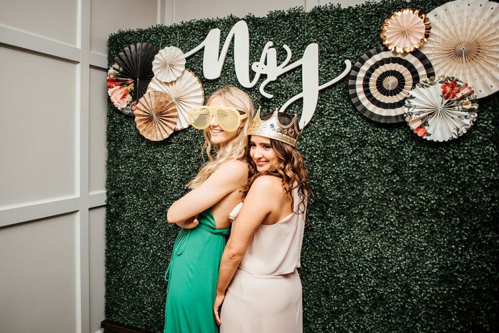 two women posing in front of a faux hedge backdrop