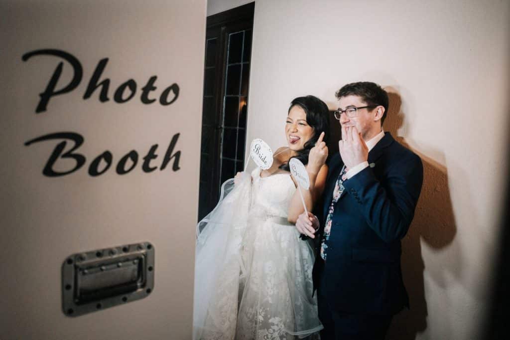 Bride and groom flashing their wedding rings in photo booth pose.